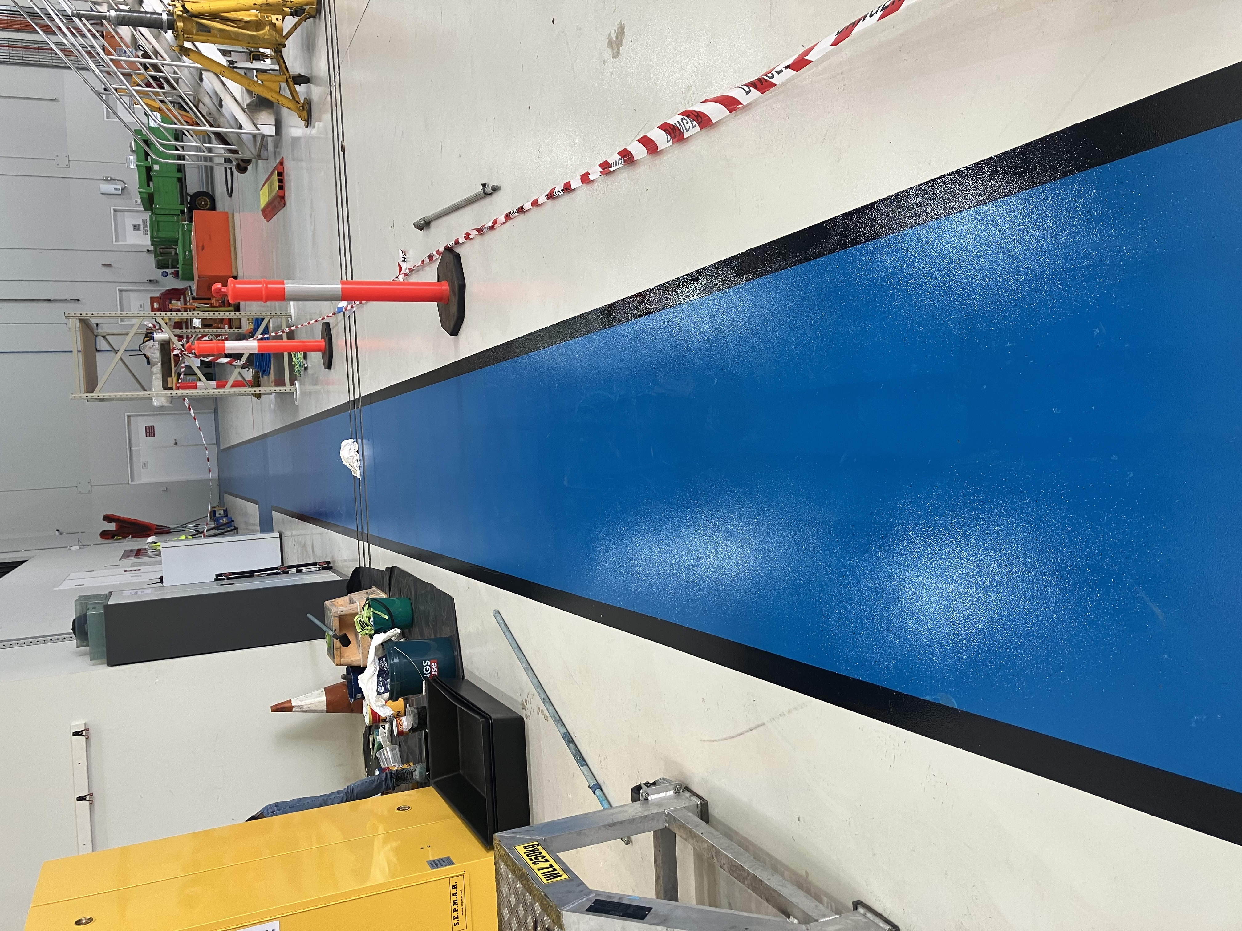 Operator using walk-behind shot blaster to remove old coatings from warehouse concrete floor during surface preparation